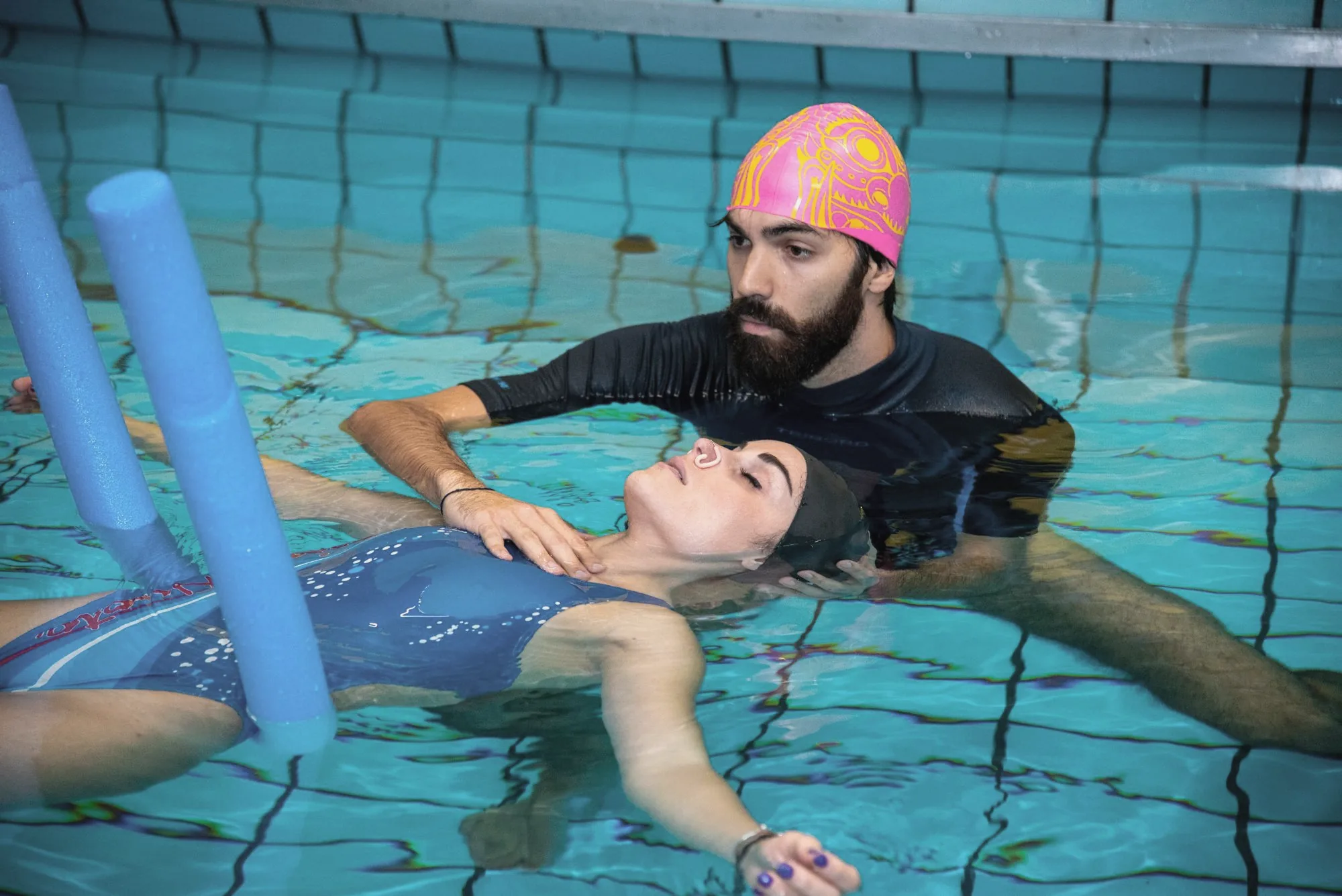 In piscina, Alessandro accompagna una persona che galleggia sulla schiena, sostenuta da galleggianti