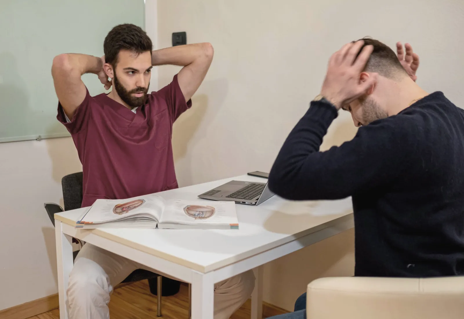 Nello studio: Alessandro mostra un esercizio a una persona seduta al tavolo, con un atlante di anatomia aperto